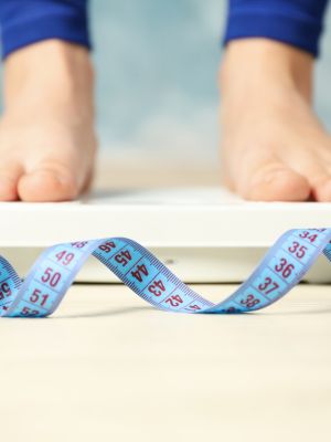 woman standing on a scale with a tape measure on the floor, thinking about her weight