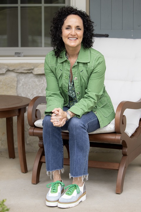 Julie James, FDNP sitting on her front porch earing a bright green jacket and colorful Office of Angela Scott oxford shoes