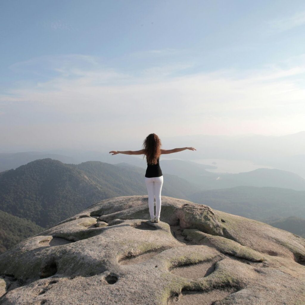 Woman standing at the summit of a mountain top exhilirated by her accomplishment of climbing the mountain