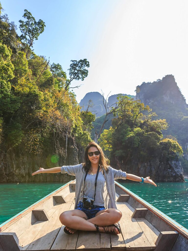 woman with camera sitting on a boat and enjoying the view of the water, trees and mountains