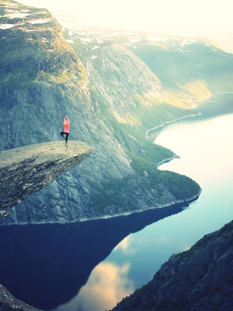 woman at the top of a mountain, overlooking the water, doing the tree pose